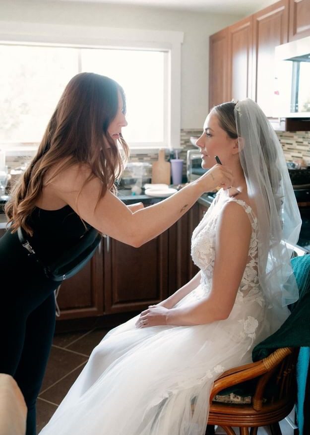 Bridal makeup artist providing last-minute lip touch ups to a bride in her wedding gown.